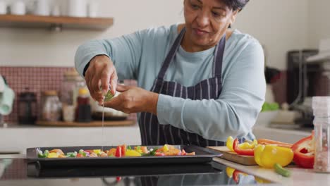 mujer asiática mayor vertiendo aceite de oliva sobre ensalada de verduras en la cocina en casa
