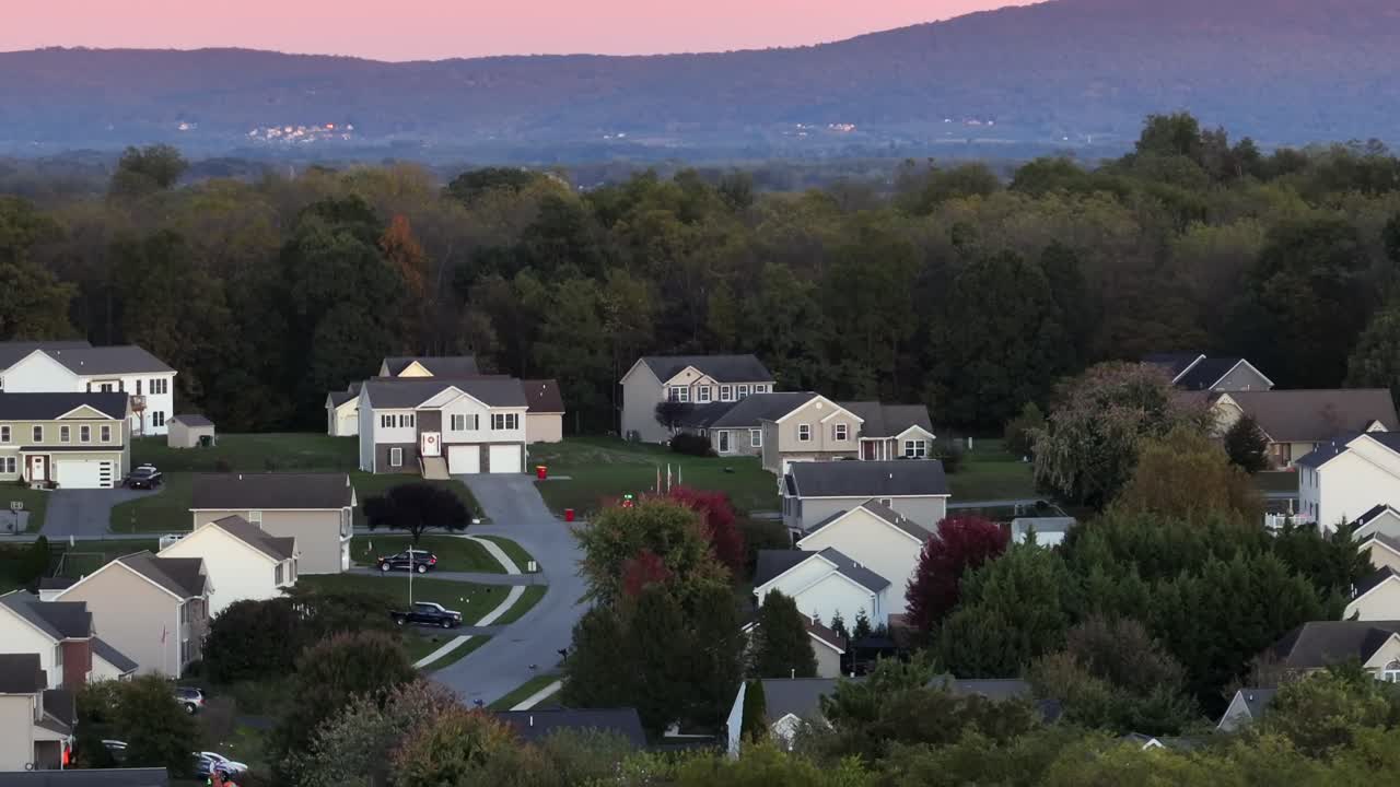 American residential area with single family houses and garage during foggy sunset time. Autumn season with colored trees and mountains in distance. Aerial wide shot. Peaceful evening in USA