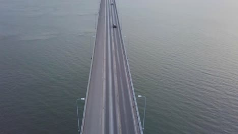 aerial tilt, top down view of cars going over massive grand bridge in seascape