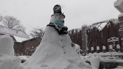 snowman wearing protection mask standing outdoors on a snowy winter day - covid protection concept - wide shot