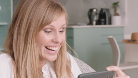 beautiful blonde woman having video chat using smartphone laughing looking surprised enjoying good news chatting to friend on mobile phone at home