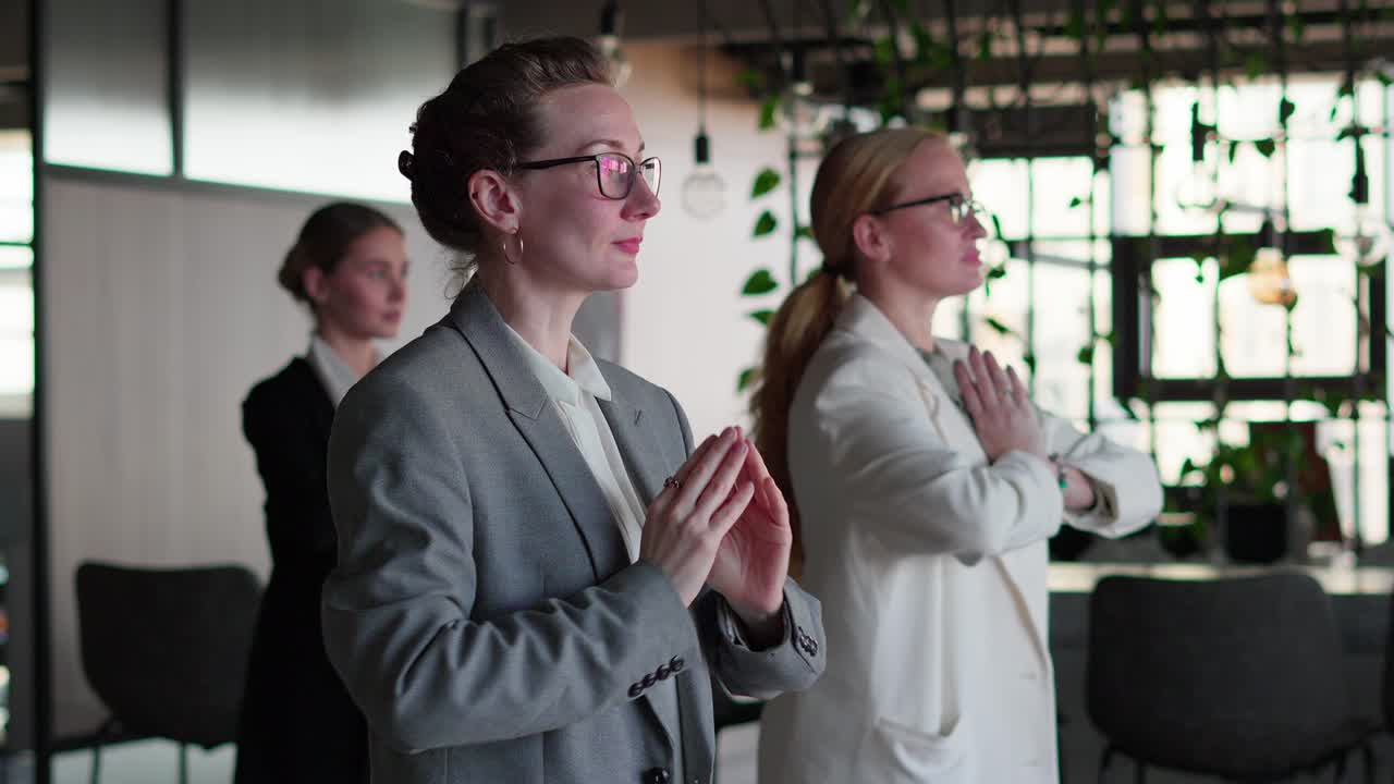vista lateral de un grupo confiado de mujeres de negocios en ropa de negocios haciendo yoga durante un breve descanso entre el trabajo en una oficina moderna