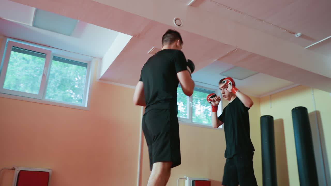 Wrestlers facing each other in boxing sparring session inside gym, one man in red gloves preparing to strike while opponent in black gloves stands ready, showing combat readiness