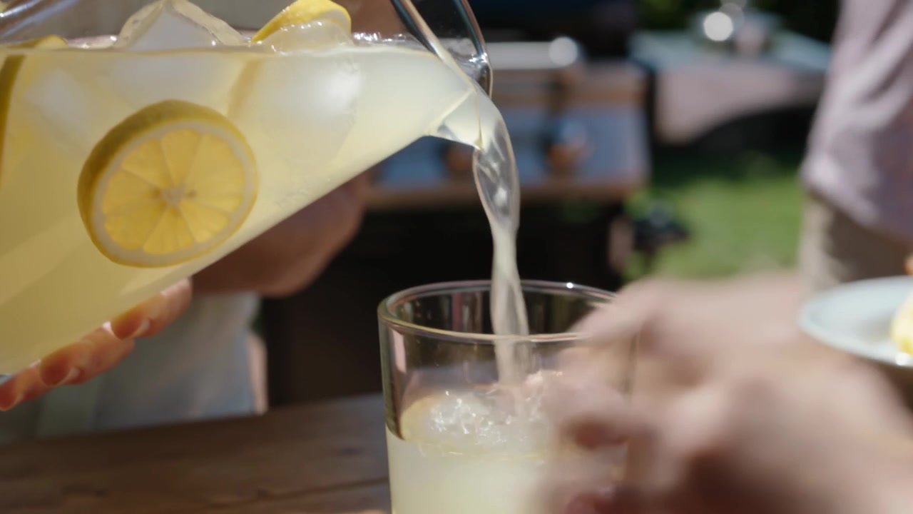 Donna anziana in canottiera che inclina la brocca versando limonata in un bicchiere in giardino per darla a un'amica.