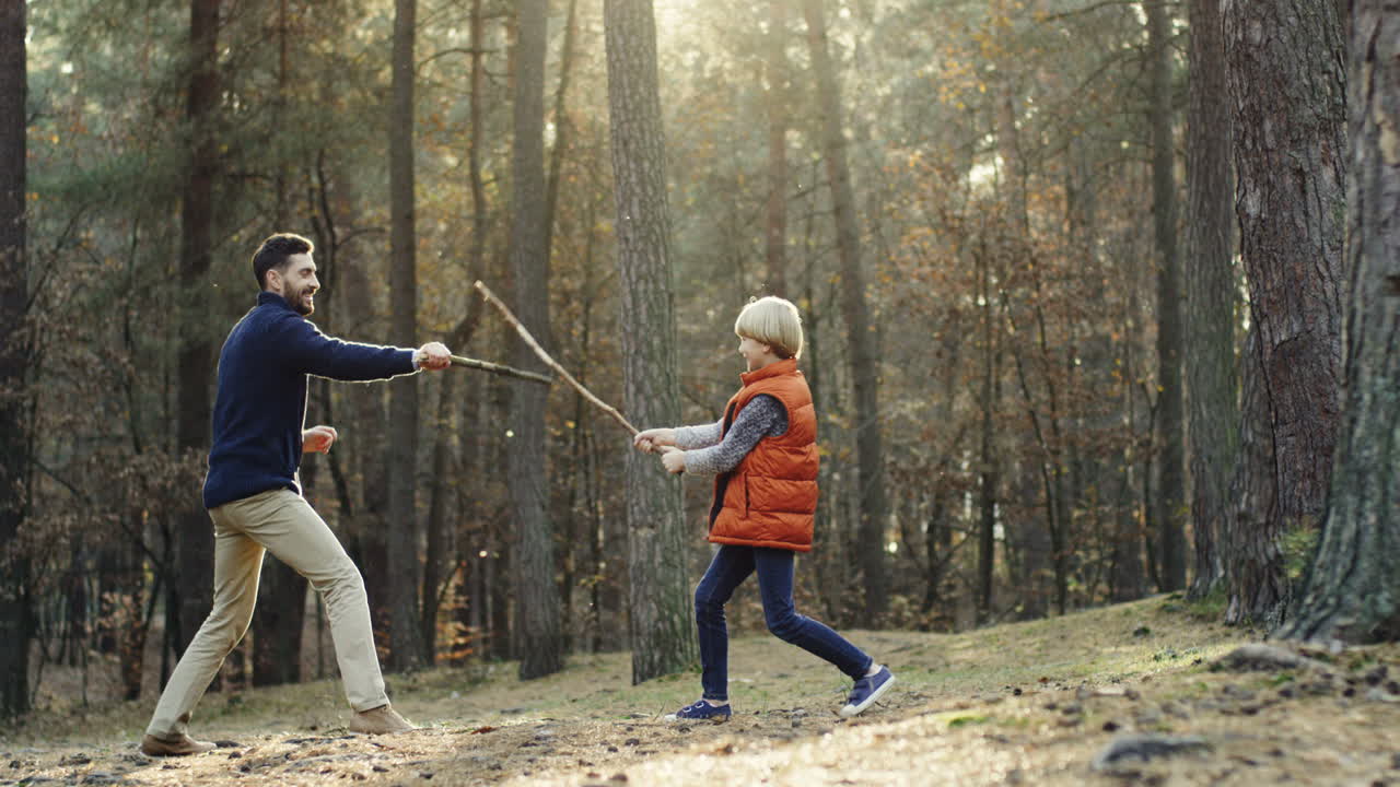Cheerful Caucasian father and little son playing in the forest with sticks like they fighting with swords