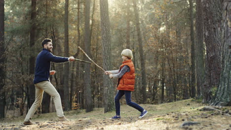 cheerful caucasian father and little son playing in the forest with sticks like they fighting with swords