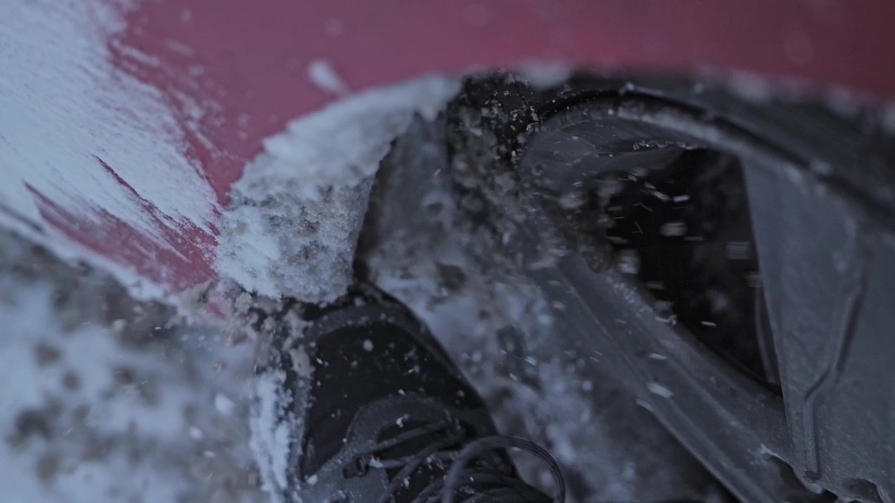 Nærbillede i slowmotion af sammenpresset is, der brydes fra en hjulkasse efter kørsel i sne.