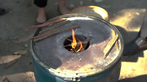 burn barrel with wooden sticks during daytime on farm with community people