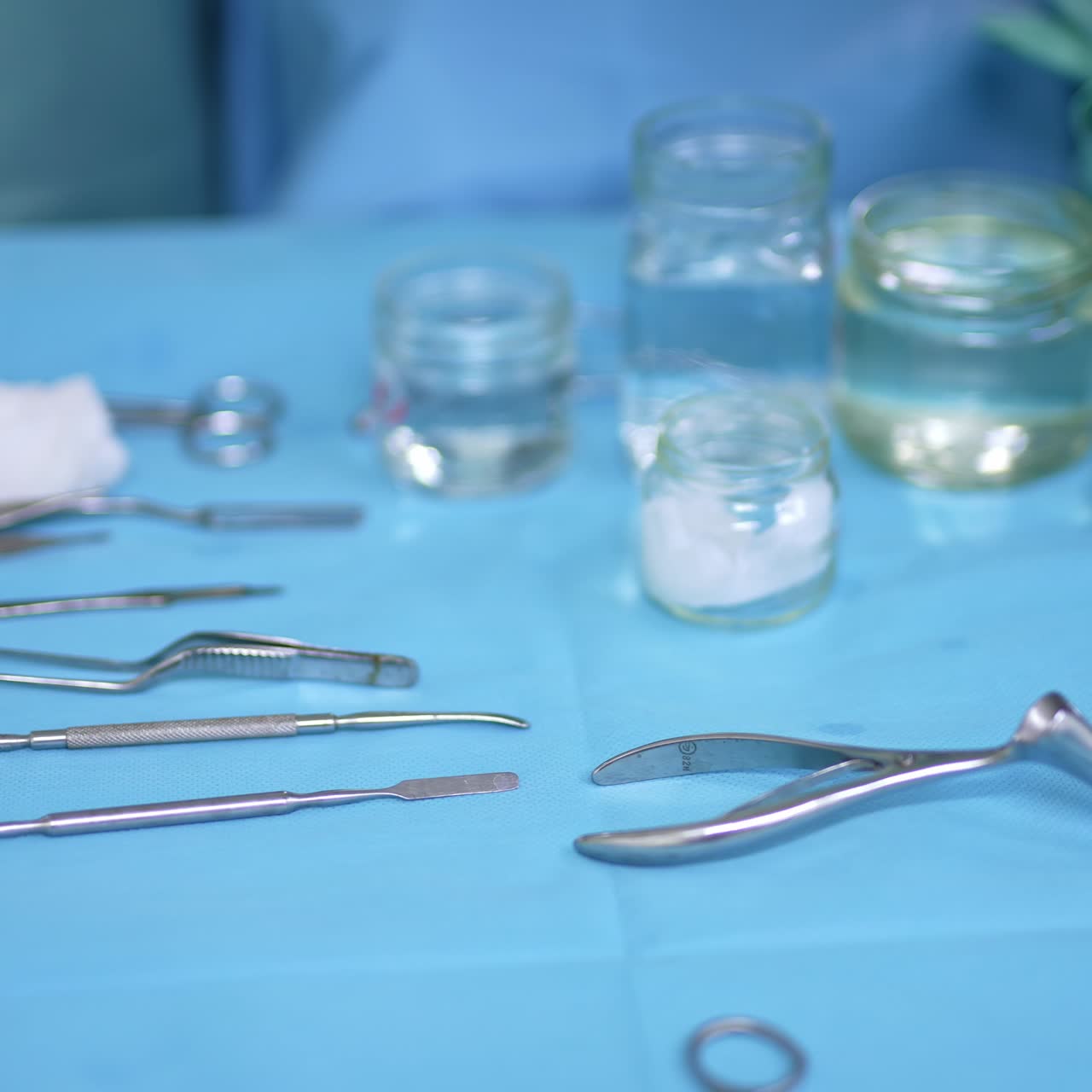 Table with metal instruments and glass jars for nasal operation. Gloved hand of a surgeon takes metal tool from a table and then sponge. Close up