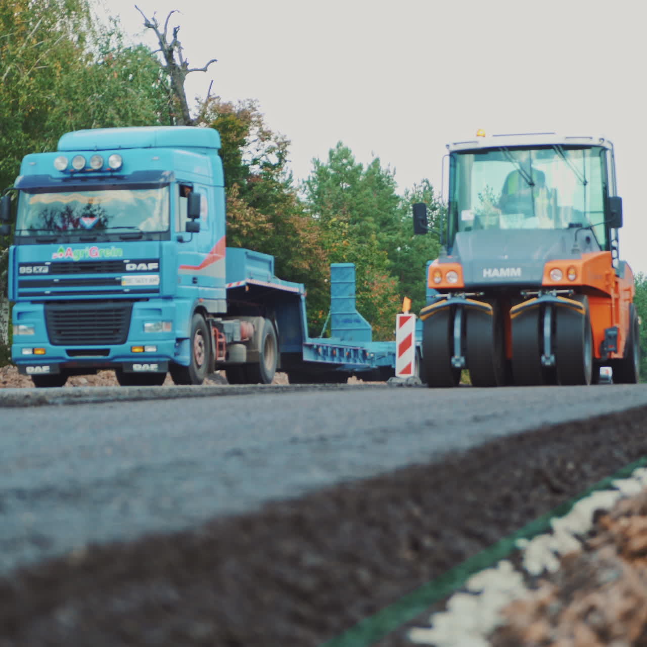 Modern asphalt roller press hot asphalt while making a new road in autumn. Road repair machine with heavy vibration rollers is working on one side of the road and other machinery going by.