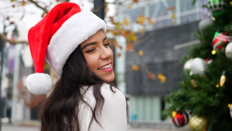 an attractive woman in a santa hat on the naughty list in front of a christmas tree with ornaments and holiday decorations