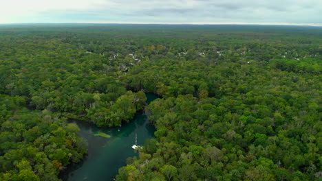 Imágenes-Aéreas-De-Un-Río-Que-Atraviesa-Un-Vasto-Bosque-Tropical-Con-Un-Barco-De-Vela-Y-Algunas-Casas-A-Lo-Lejos,-Dolly-En-La-Toma