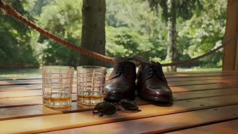 whiskey glasses, shoes and sunglasses on a table with a garden background.