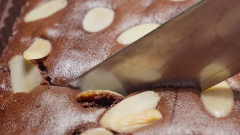 el cuchillo de metal corta a través del chocolate y el pastel de almendras, primer plano extremo