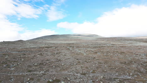 aerial shot of high plateau mountain landscape, glaciers and snow tops on the horizon, panoramic push in movement of a surreal moon landscape, blue sky and pretty clouds