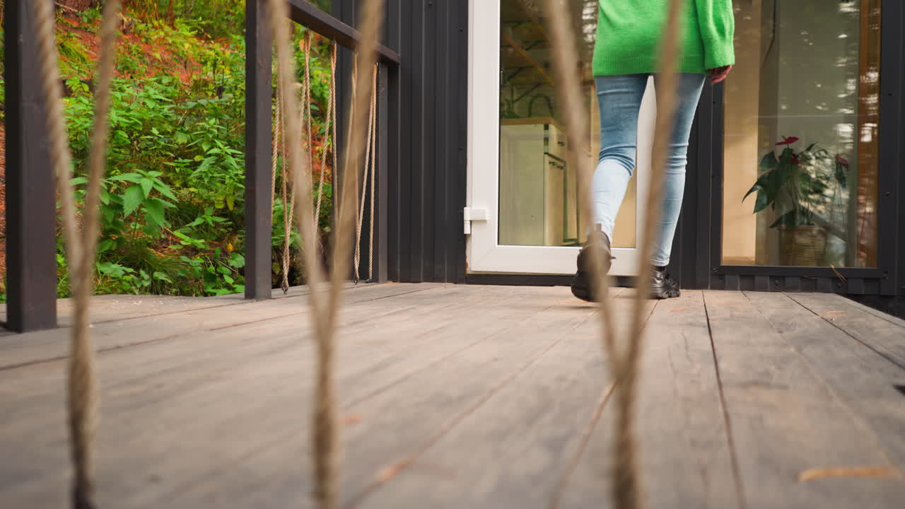 dama entra en casa de glamping después de caminar. joven camina con confianza a la entrada de la cabaña después de caminar en el bosque. vacaciones en la ciudad de cabañas durante el otoño. vista a través de la valla de cuerda