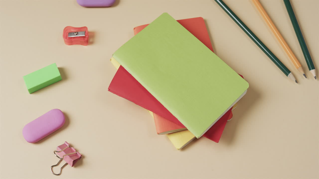 primer plano de cuadernos coloridos con papelería escolar en fondo beige, en cámara lenta