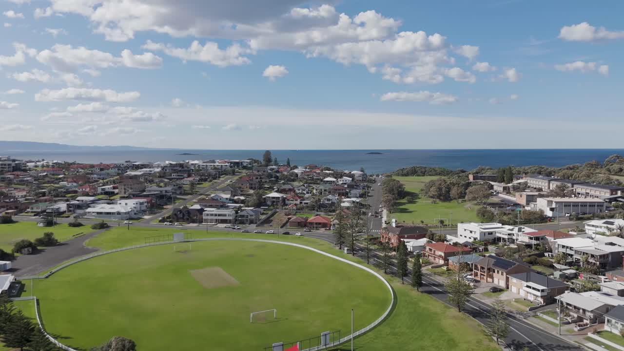드론은 럭비 피치와 함께 주차장과 놀이터 위로 상승하여 포트 블라, nsw, 오스트레일리아에서 바다를 바라보는 주택을 드러니다.