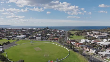 drone ascends above parking lot and playground with rugby pitch to reveal oceanfront homes looking to see in port kembla nsw australia