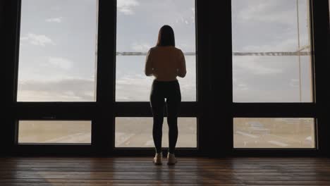 Still-woman-stand-near-wide-window-pane-in-multistory-building-and-look-outside