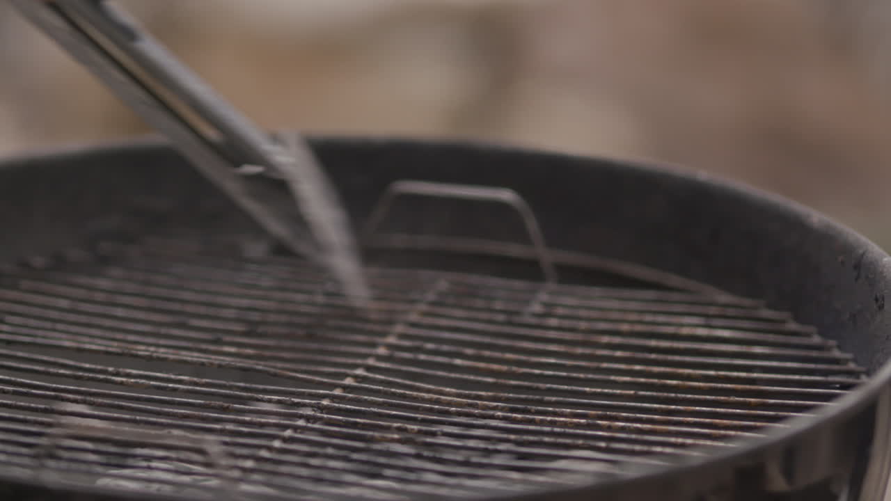 Raschiare e pulire un barbecue a carbone nero con pinze di metallo