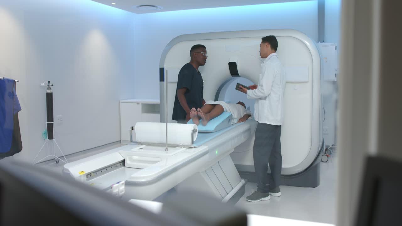 Equipe medica che sistema una paziente donna sul lettino nella sala dello scanner dopo che il medico ha controllato il tablet.