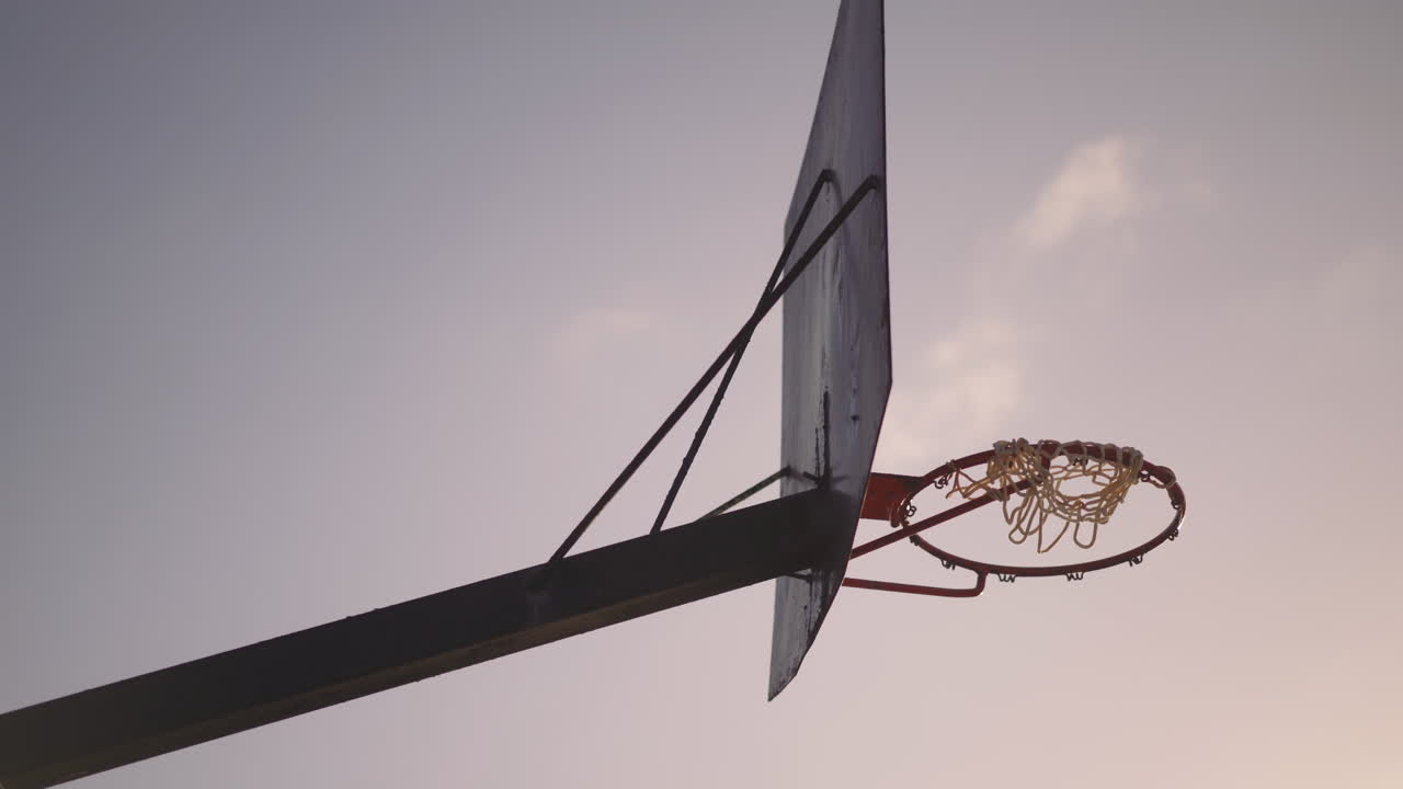 Old rusty basketball hoop with torn net hanging in wind at sunset