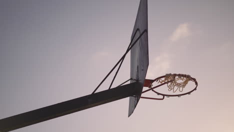 old rusty basketball hoop with torn net hanging in wind at sunset