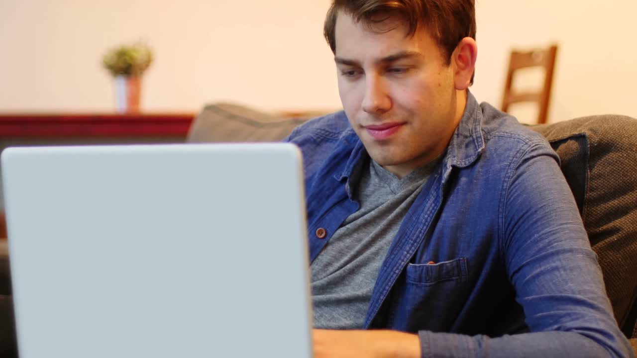 hombre sentado en el sofá y usando computadora portátil en la sala de estar