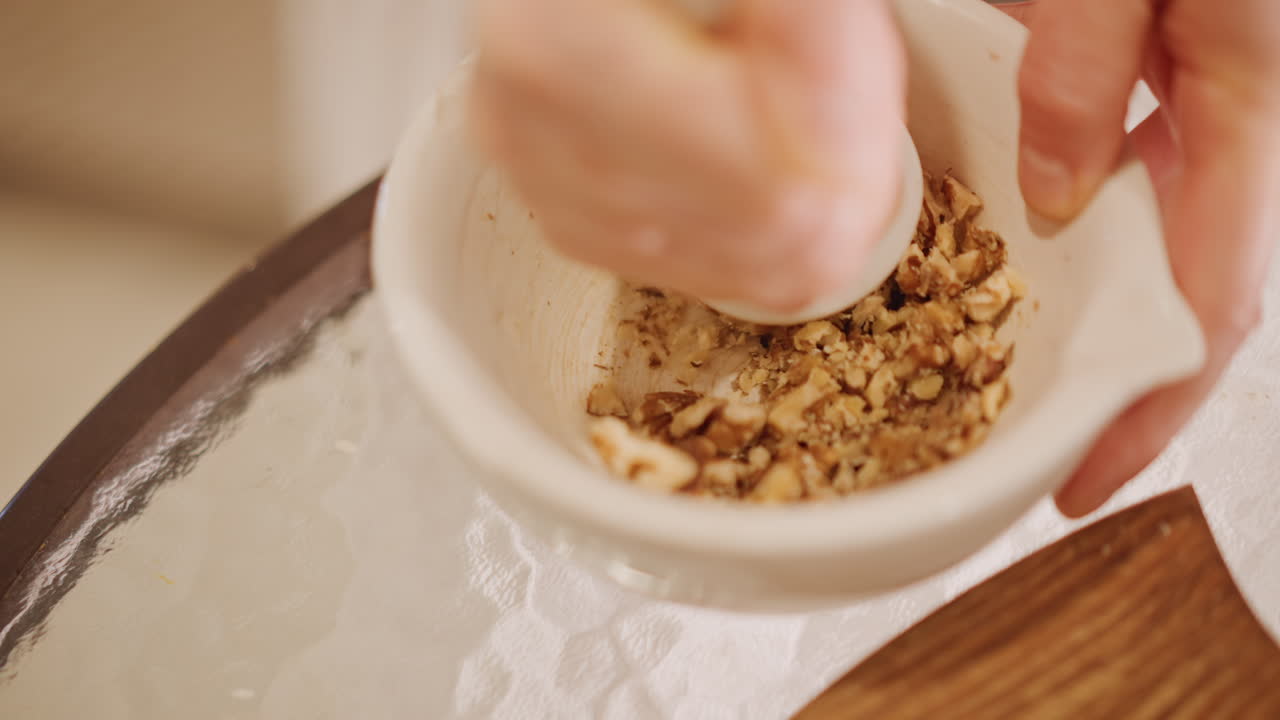Primo piano di mortaio e pestello che macinano, mani che schiacciano noci in un composto friabile per la crosta della torta di zucca, texture tattile e movimento ritmico, luce naturale calda, preparazione artigianale focalizzata