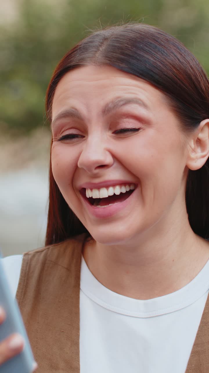 joven europea emocionada usando su teléfono inteligente escribiendo navegando celebrando la victoria en la calle de la ciudad urbana