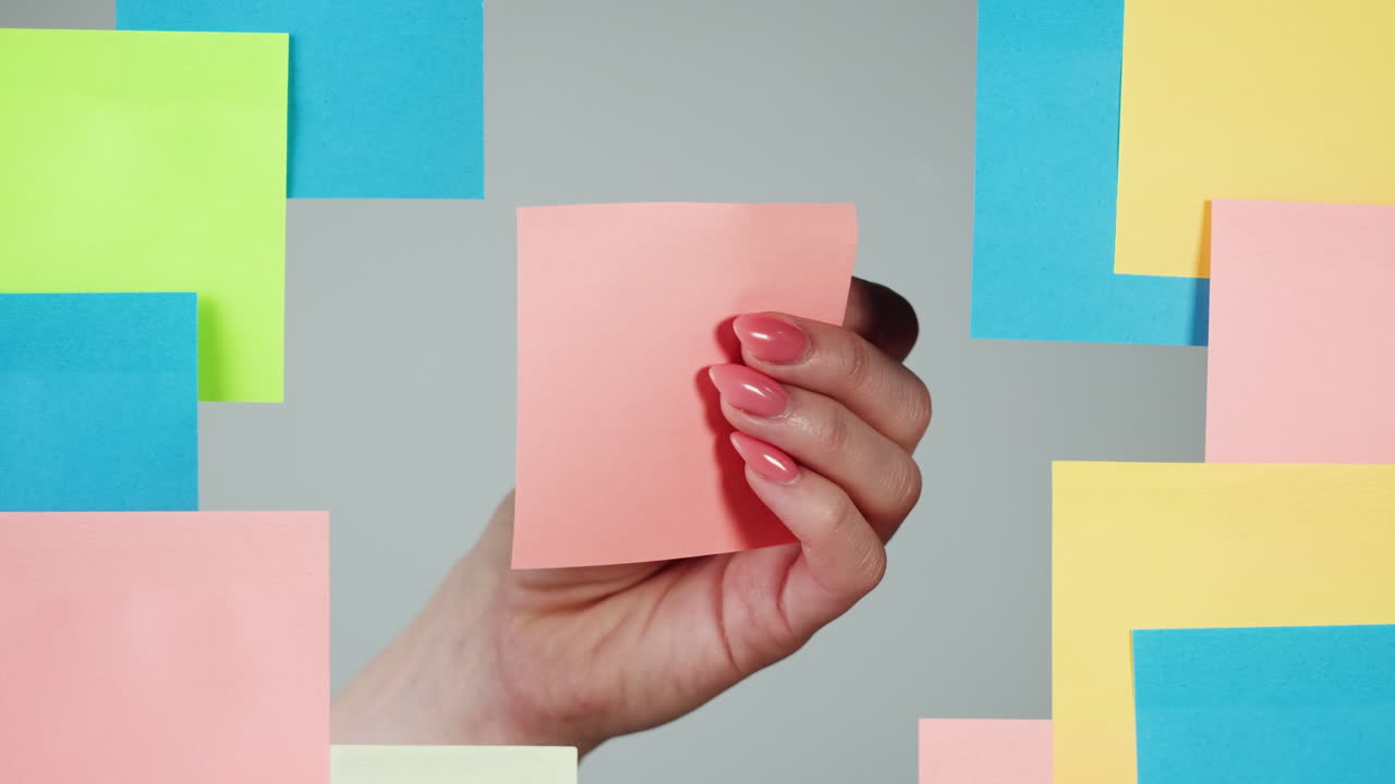 Female Hand Placing a Pink Sticky Note Among Colorful Notes