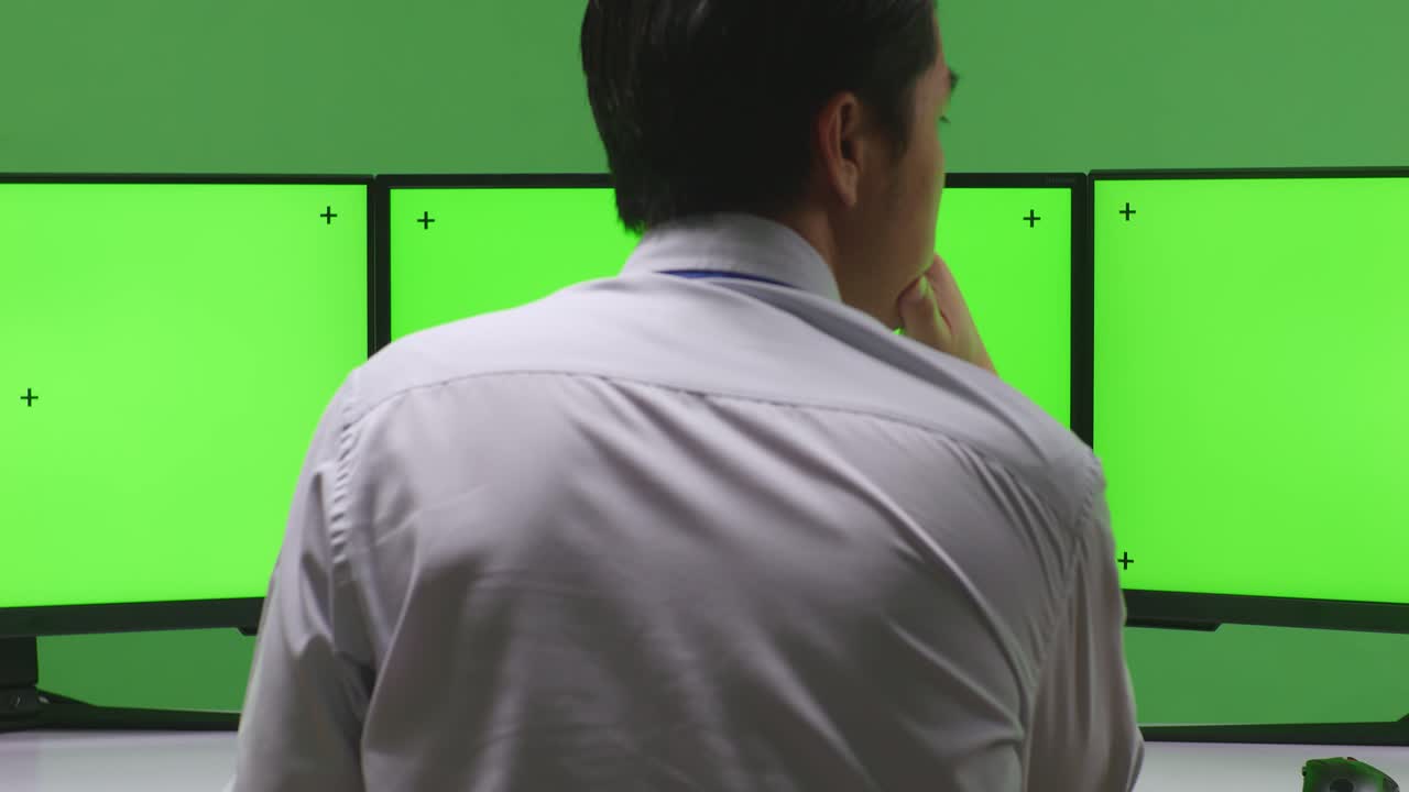 녹색 화면 을 가진 여러 모니터 를 보고 있는 사무실 의 사업가