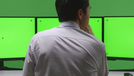 hombre de negocios en una oficina mirando múltiples monitores con pantallas verdes