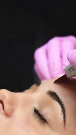 woman receiving cleansing therapy with a professional ultrasonic equipment in cosmetology office. vertical video