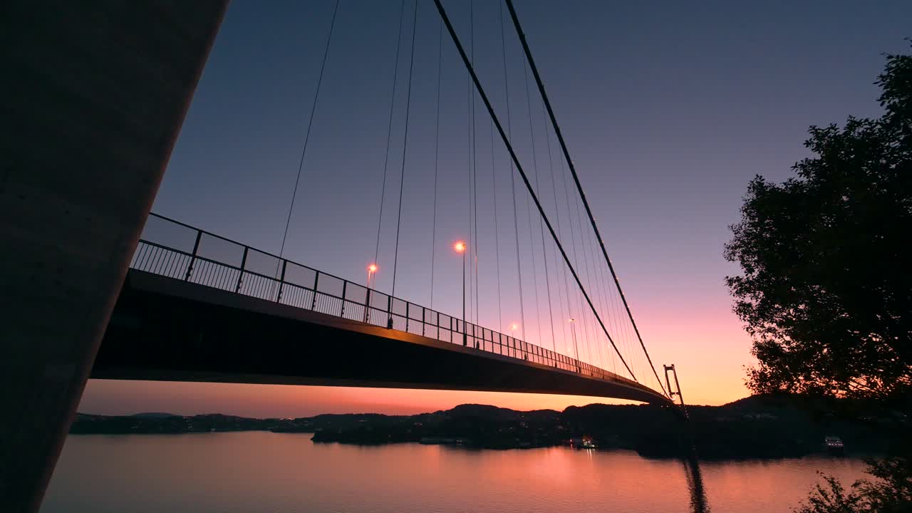 el cielo de la puesta de sol de verano ilumina el horizonte y se refleja en el agua bajo el puente askoy