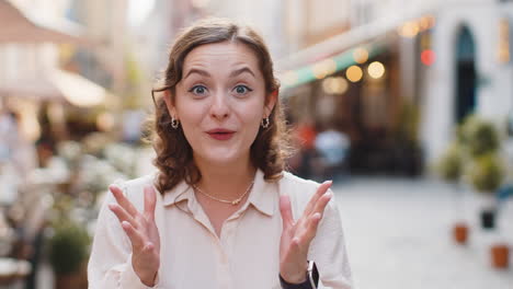 young woman looking surprised at camera shocked by sudden win good victory news, wow in city street