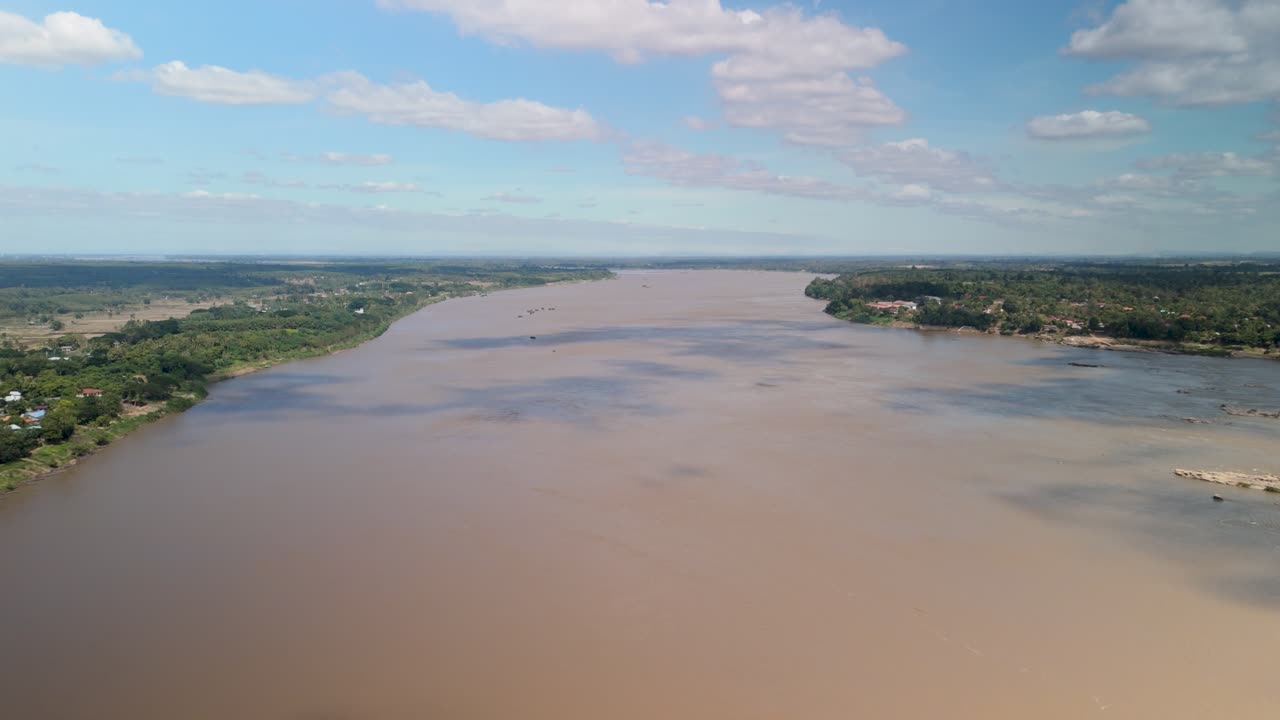 Drone panorama of the broad muddy Mekong with farms and villages lining the banks under scattered clouds