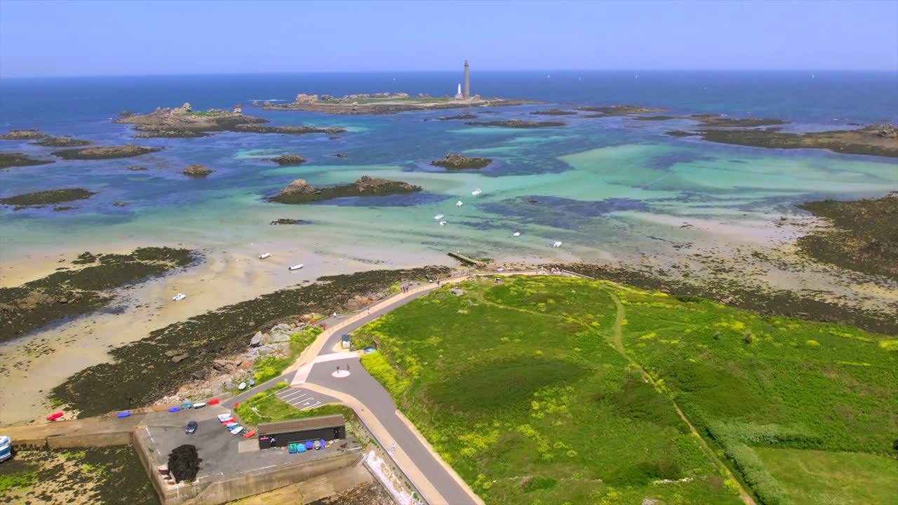 Drone footage showcasing the vibrant Brittany coastline with rocky islands, shallow turquoise waters, a historic lighthouse, and green coastal paths. Perfect for travel and nature visuals.
