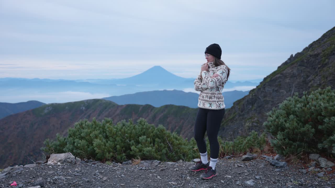 Young caucasian woman in beanie stading on a viewpoint looking at Mt. Fuji from Mt. Kitadake, Japanese Alps