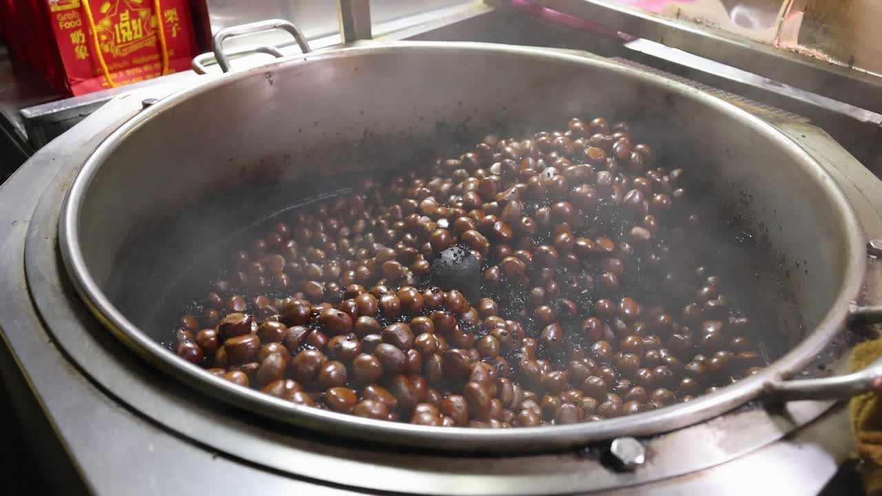 Chestnuts roasting in a steaming metal pan, street food style, under warm ambient lighting