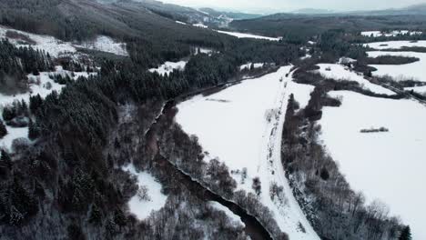 Circle-pan-aerial-drone-view-of-magnificent-snowy-white-countryside-landscape-river-forest,-rising-up,-Slovakia-High-Tatra,-cloudy-day