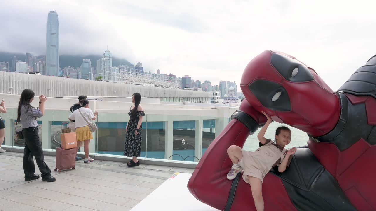 In Hong Kong, a child poses beside an 8-meter Deadpool statue while onlookers snap photos. The giant display promotes Disney's "Deadpool and Wolverine" movie.
