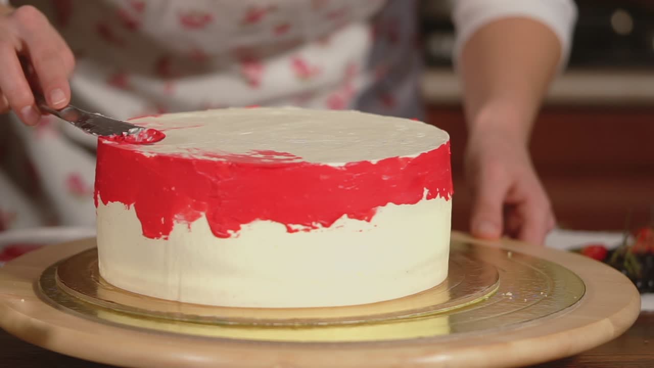 donna che decora una bella torta bianca con glassa rossa