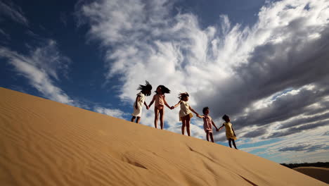 girls holding hands walking up a sand dune
