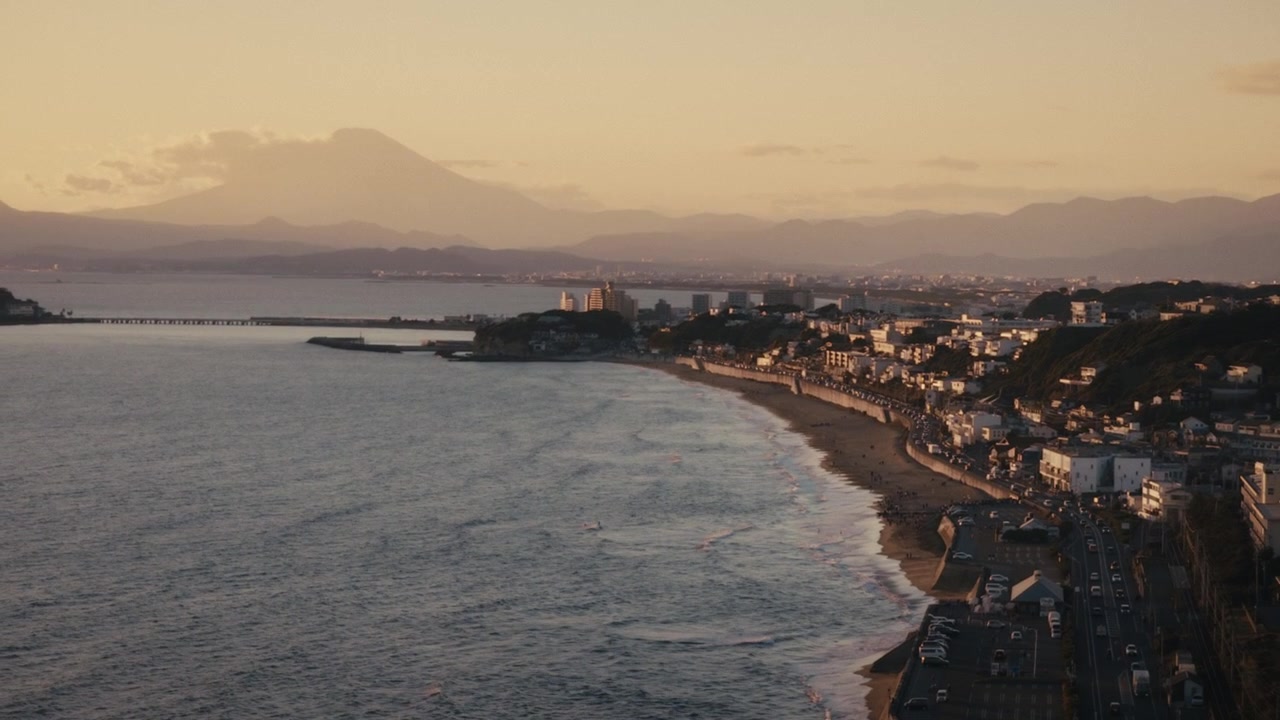 Vista aerea della costa di Shichirigahama al tramonto, Kamakura, Giappone, con il Monte Fuji che si erge sopra la Baia di Sagami e case collinari che costeggiano la riva