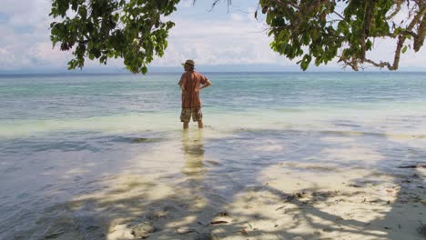 man standing in the calm tropical waters of a serene beach