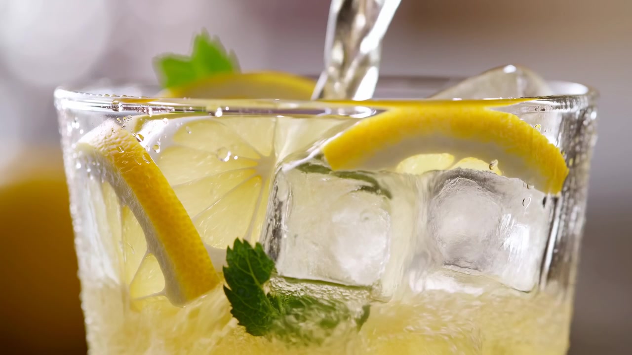 Nærbillede af glas med is og citron, slowmotion hældning skaber kondens og stænk, frisk mynteblad og lyst