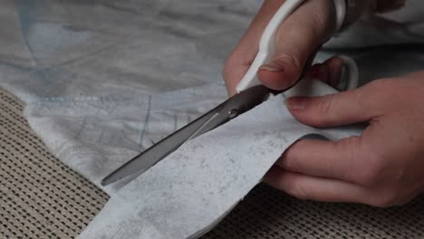 closeup of young woman hands carefully cutting light blue fabric cloth material with white scissors