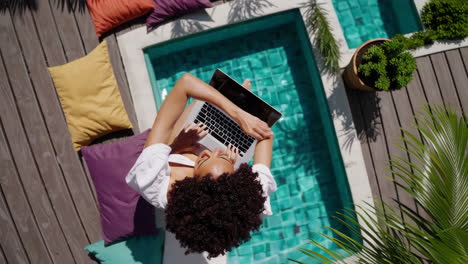 woman working on a laptop by a tropical pool from an overhead view